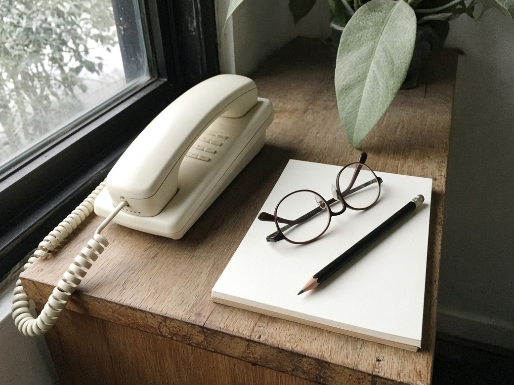 Cream landline, blank paper, glasses and a pencil on a timber ledge