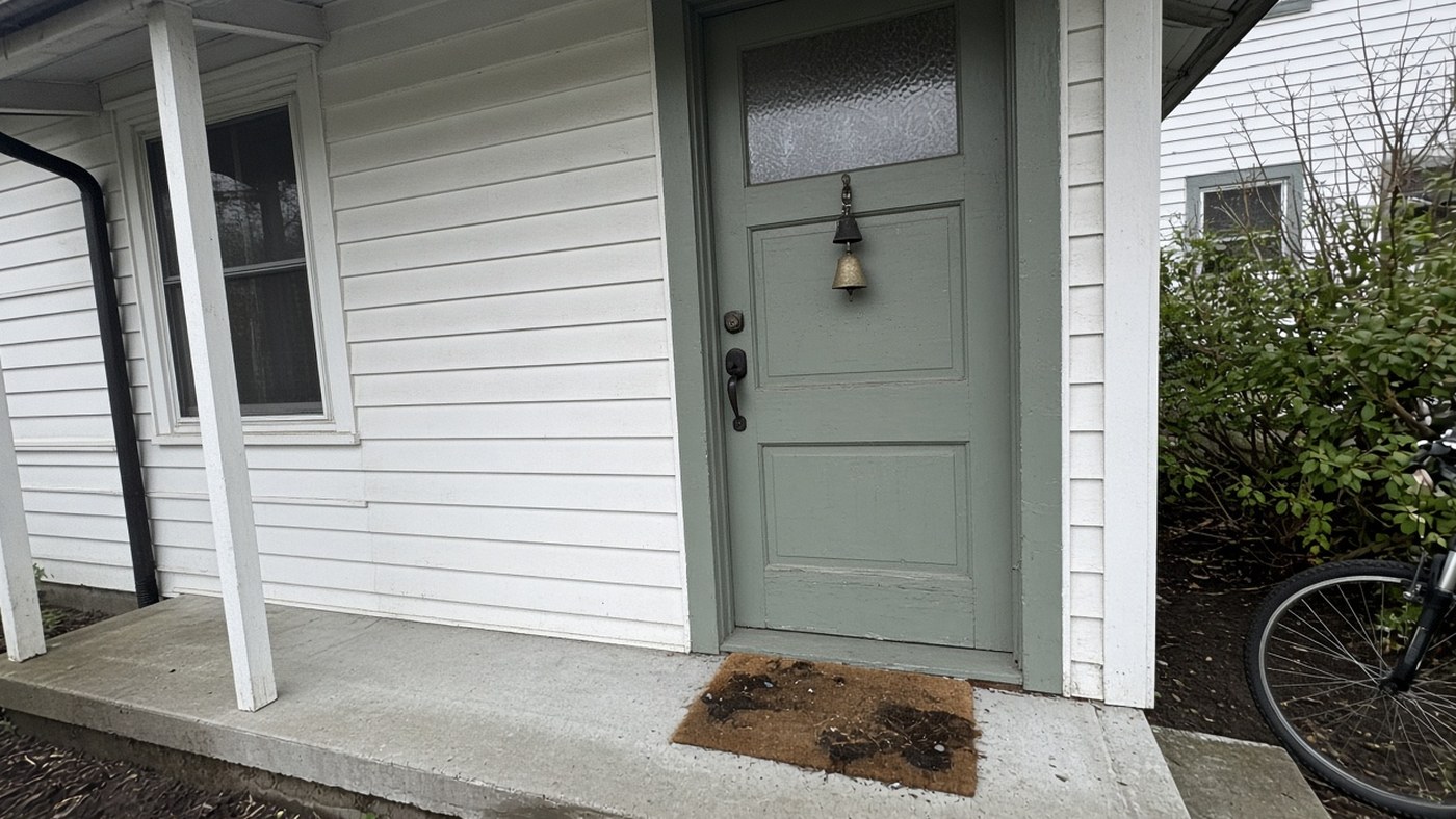Sage wooden side door with two small bells and a muddy coir mat