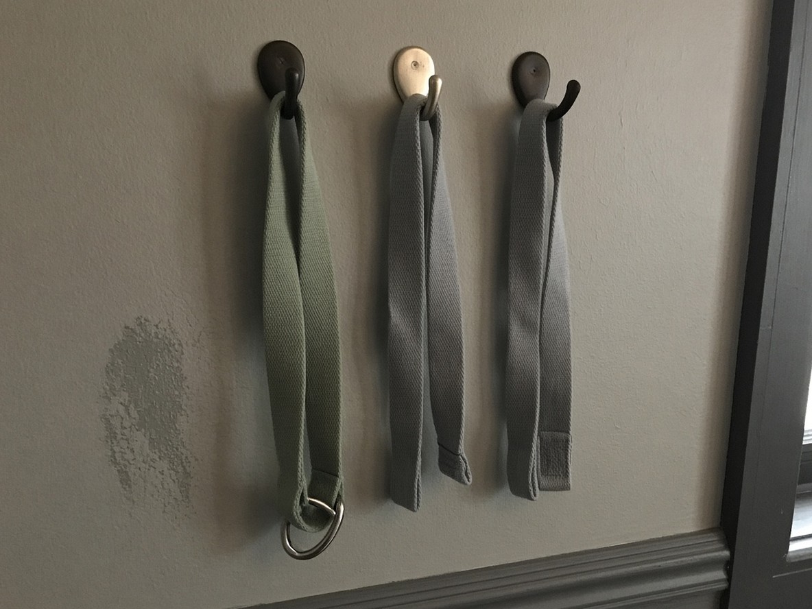 Three cotton yoga straps hanging from mismatched wall hooks
