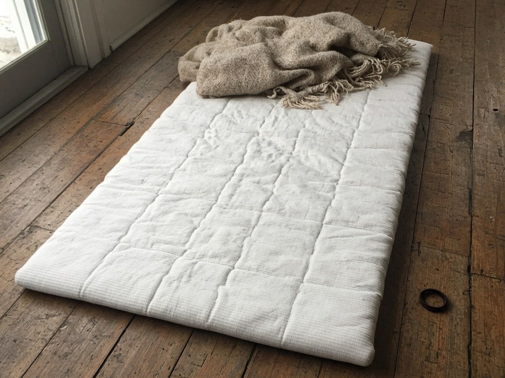 One cotton mat with a rumpled blanket on worn timber boards